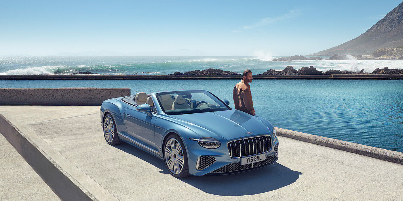 Bentley Kuwait New Bentley Continental GTC Azure convertible front view in Light Windsor blue paint with 22 inch ten spoke wheels parked by the sea in the sunshine
