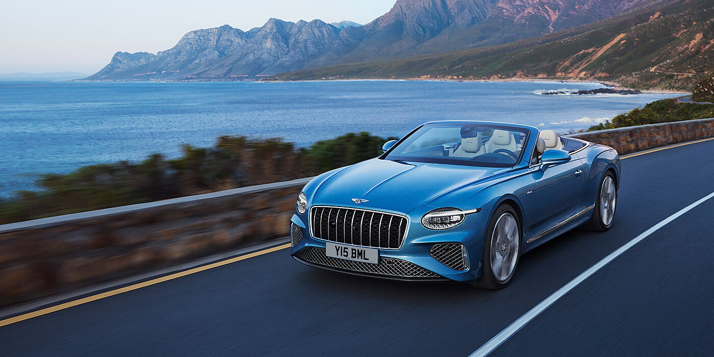 Bentley Kuwait New Bentley Continental GTC Azure convertible in Light Windsor blue paint with 22 inch Azure wheels and chrome grill, driving dynamically by the sea