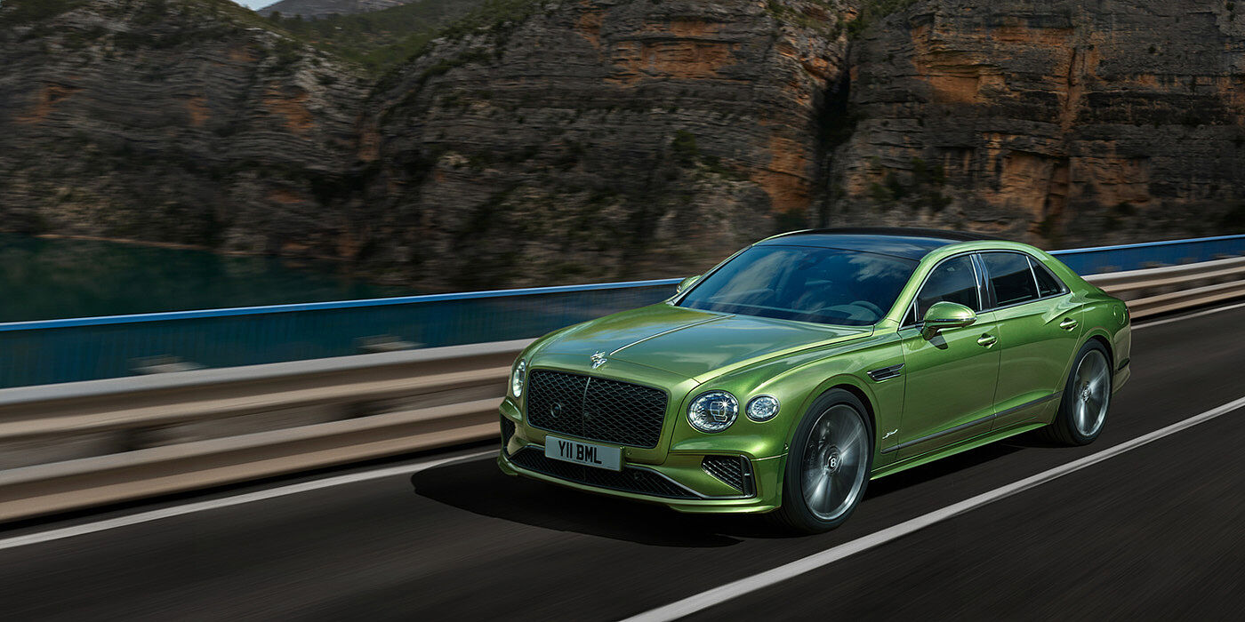 Bentley Kuwait Bentley New Flying Spur Speed v8 hybrid sedan driving dynamically on a mountain road in Tourmaline Green paint