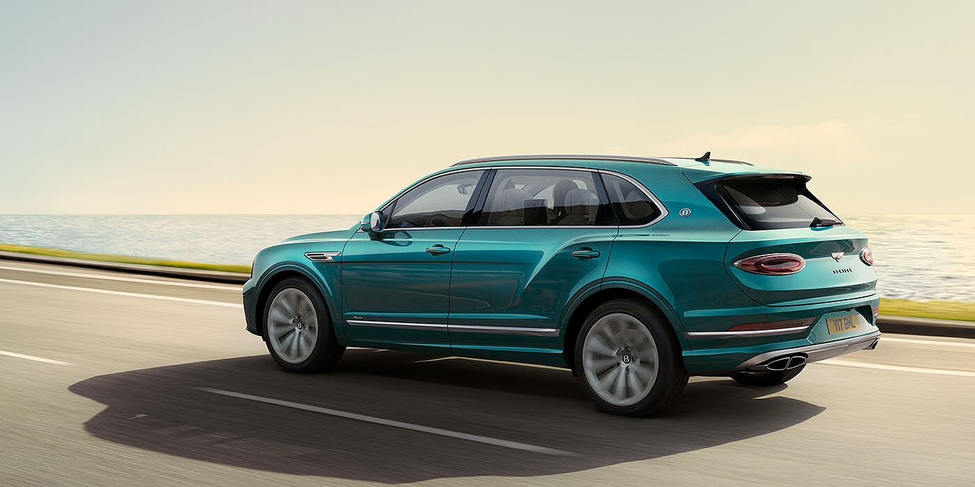 Bentley Kuwait Bentley Bentayga Extended Wheelbase Azure luxury SUV rear three quarter in Topaz Blue by Mulliner paint, driving on an ocean road.