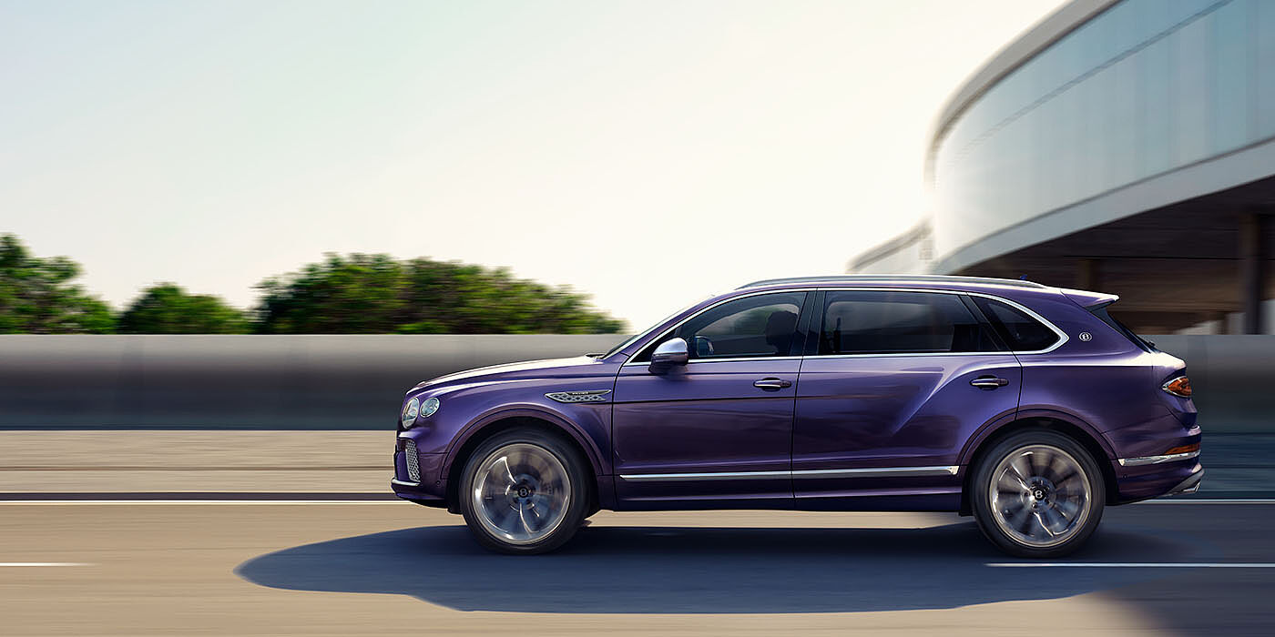 Bentley Kuwait Bentley Bentayga Extended Wheelbase Mulliner luxury SUV profile in Tanzanite Purple paint, driving on an country road past trees.