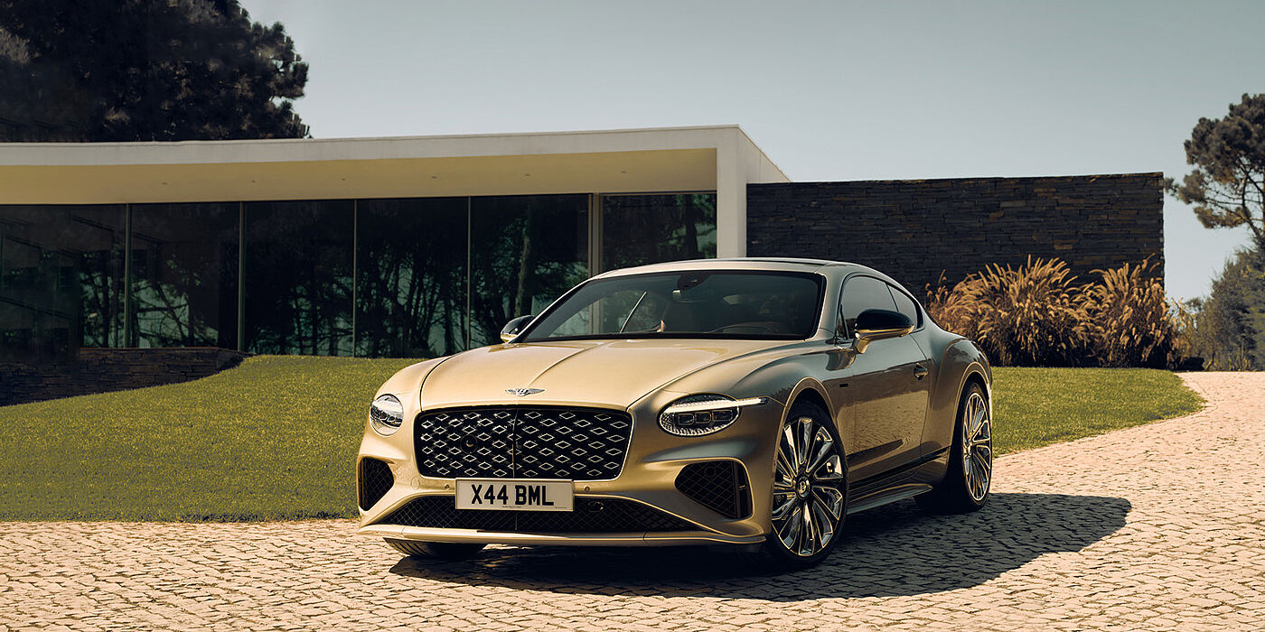 Bentley Kuwait Bentley Continental GT Mulliner coupe front three quarters in Patina paint parked outside a glass fronted building with a grass lawn behind it