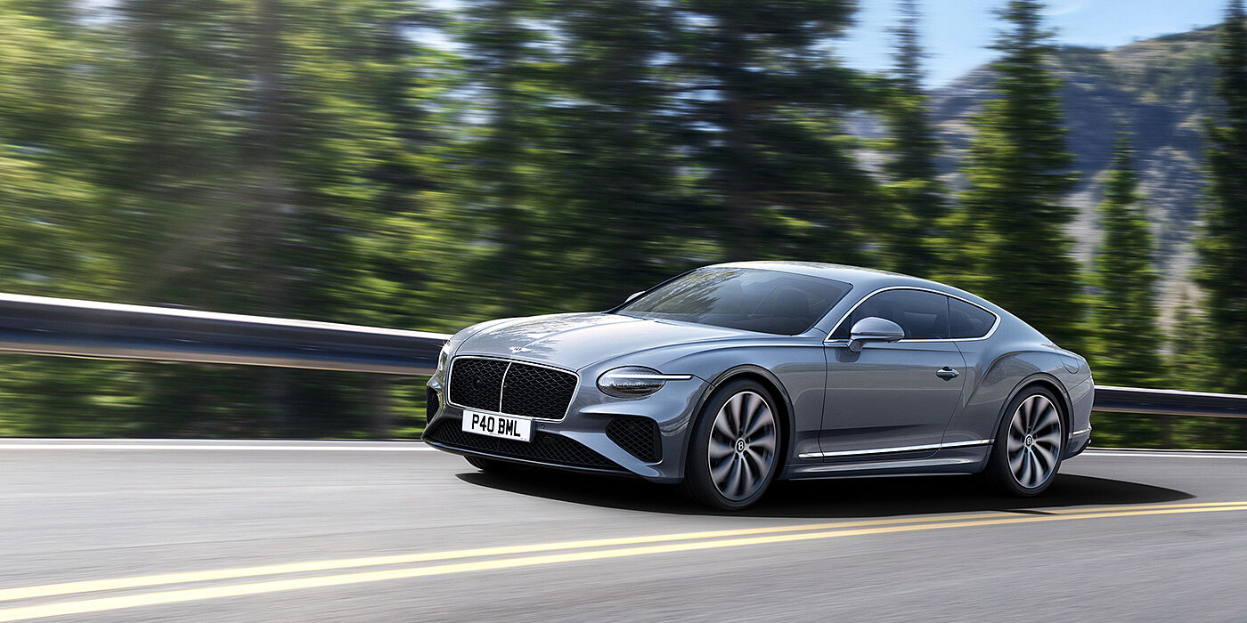 Bentley Kuwait New Bentley Continental GT coupe in Silverlake paint and 22 inch ten-spoke wheels, driving dynamically on a tree-lined road in the sunshine