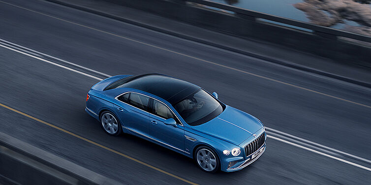 Bentley Kuwait New Bentley Flying Spur Azure sedan in Light windsor blue paint by Mulliner, with 22 inch Azure wheels seen from overhead driving dynamically on a country road
