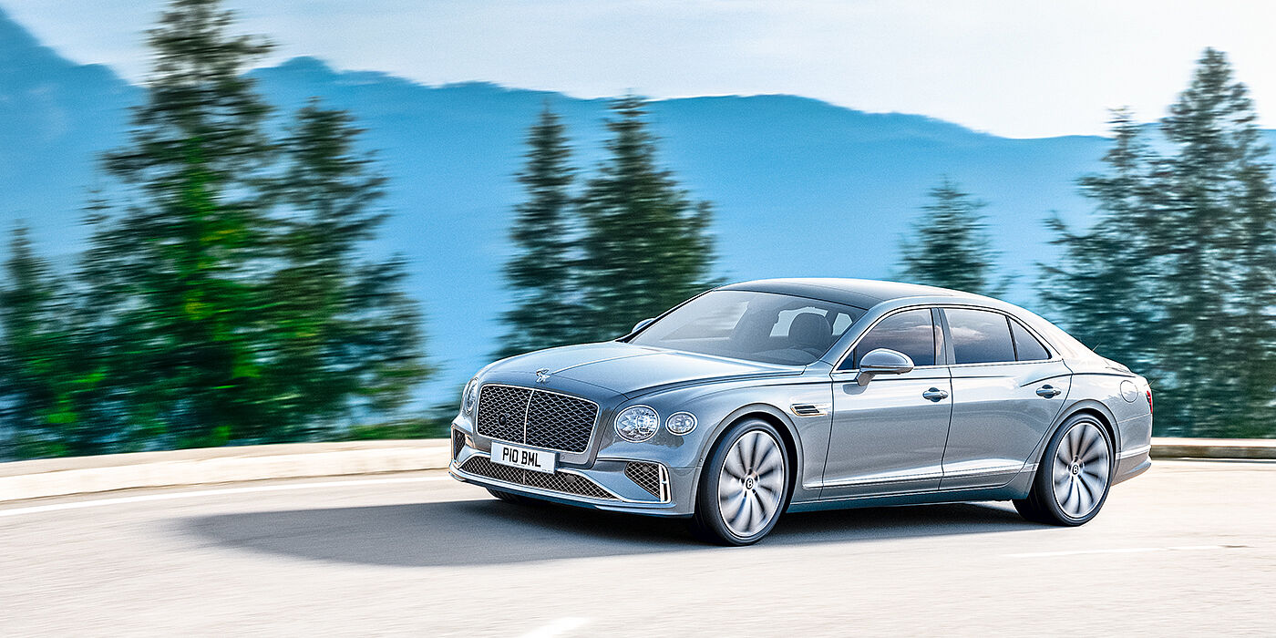 Bentley Kuwait New Bentley Flying Spur sedan side view in Silverlake paint with ten spoke wheels and chrome matrix grille driving dynamically on a mountain road