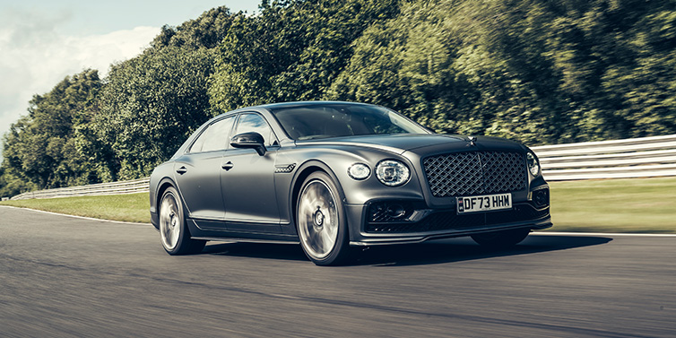 Bentley Kuwait Bentley Flying Spur Mulliner sedan front three quarter in dark grey paint driving dynamically by some trees on a track