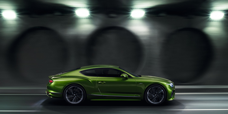 Bentley Kuwait Bentley Continental GT Speed coupe profile in Tourmaline Green driving dynamically past a concrete wall at night