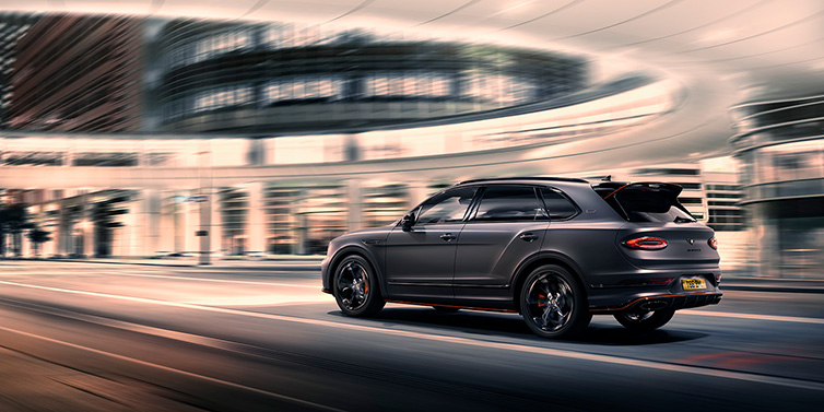 Bentley Kuwait Bentley Bentayga S Black Edition SUV rear three quarter in Anthracite Satin paint driving dynamically through a city at night