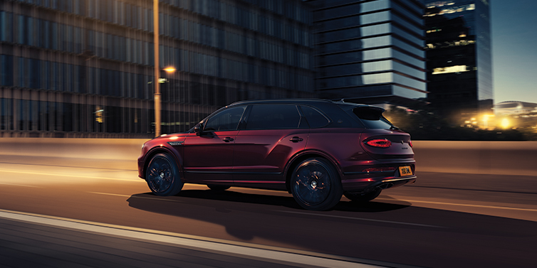 Bentley Kuwait Bentley Bentayga Extended Wheelbase Mulliner SUV in Cricket Ball red paint driving dynamically in city at night