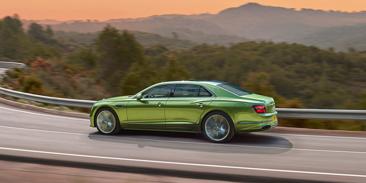 Bentley Kuwait Bentley Flying Spur Speed sedan side profile in Tourmaline Green paint driving dynamically on a mountain road at sunset